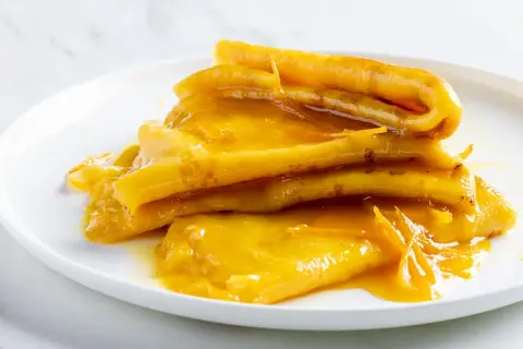 Pila di crepes suzette dorate, ricoperte da una salsa all'arancia lucida e invitante.