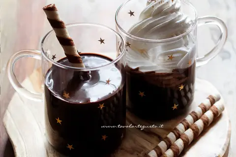 Due tazze di cioccolata calda senza fecola e senza amido, una con cialda, l'altra con panna montata e cacao.