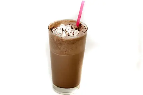 Un delizioso frappè al cioccolato, guarnito con panna montata e scaglie di cioccolato, pronto per essere gustato con una cannuccia rosa.