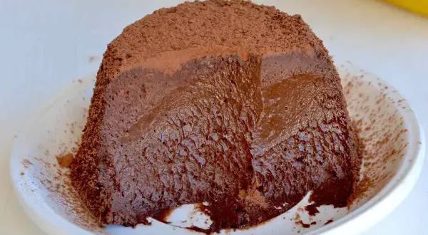 Dolce banana e cioccolato: una torta soffice e cremosa, ricoperta di cacao, servita su un piatto bianco.