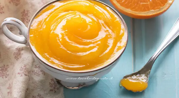 Una tazza di deliziosa crema all'arancia, con una fetta d'arancia e un cucchiaino pronto per assaggiarla.