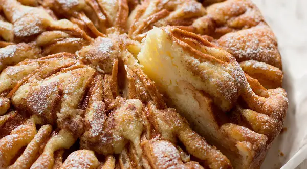 Una deliziosa torta di mele, cosparsa di zucchero a velo, con una fetta appena tolta che rivela la morbidezza dell'impasto e le mele caramellate.