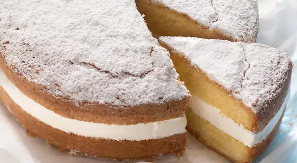 Una soffice torta kinder paradiso, spolverata di zucchero a velo, con una golosa crema bianca tra due strati di pan di Spagna.