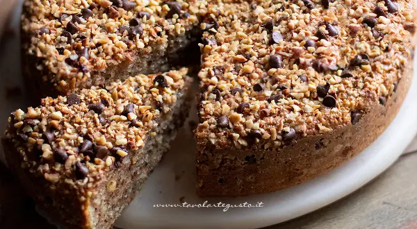 Una deliziosa torta di nocciole, ricoperta di granella croccante e gocce di cioccolato, con una fetta tagliata.
