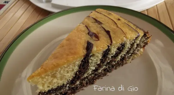 Una fetta di torta zebrata, con strati alternati di impasto chiaro e scuro, su un piatto con bordo verde.