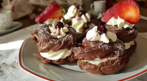 Zeppole al cacao con panna montata, ciliegie e fragole, spolverate di zucchero a velo.