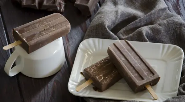 Tre ghiaccioli al cioccolato, uno su una tazza bianca, gli altri su un piatto, con pezzi di cioccolato sullo sfondo.