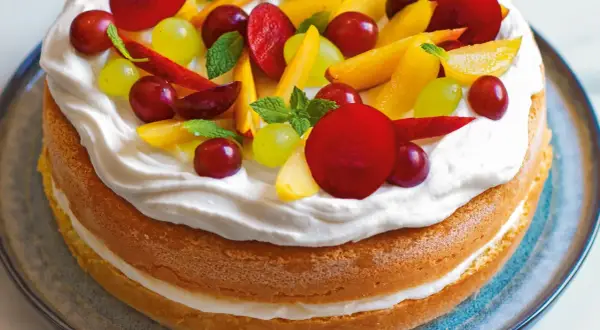 Torta con pan di spagna, panna montata e frutta fresca: uva, pesche e prugne. Un dolce estivo colorato e invitante.