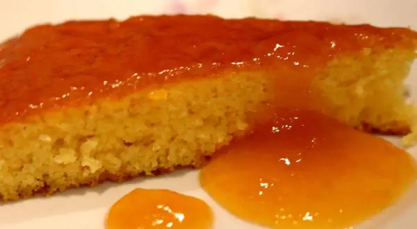 Una fetta di torta senza glutine, soffice e dorata, coperta da una lucida glassa all'arancia.