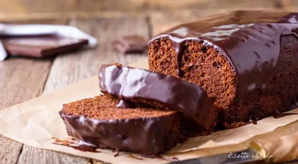 Plumcake al cioccolato con glassa lucida e due fette tagliate, su carta da forno e legno.