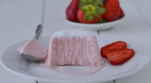 Delizioso semifreddo alle fragole, con una porzione su un cucchiaio e fragole fresche sullo sfondo.