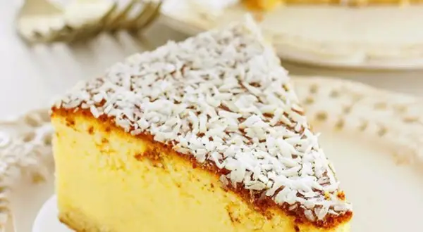 Una fetta di torta alla ricotta veloce e morbidissima, cosparsa di cocco grattugiato, su un piatto bianco.