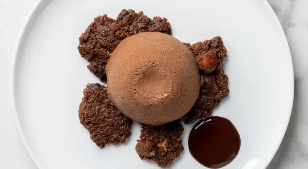 Delizioso semifreddo al cioccolato su un piatto bianco, circondato da croccanti biscotti al cacao e una goccia di salsa al cioccolato.