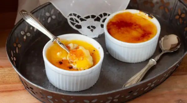 Due deliziosi creme brulee in cocotte, uno con un cucchiaino che ne assaggia la crosticina caramellata.