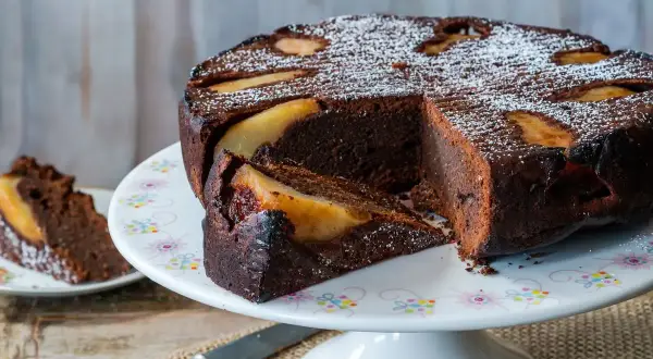 Deliziosa torta pere e cioccolato, con una fetta tagliata e cosparsa di zucchero a velo.
