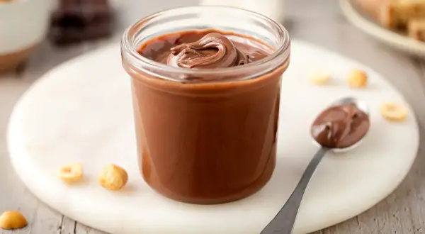 Un vasetto pieno di deliziosa nutella fatta in casa, con nocciole e cioccolato a vista.