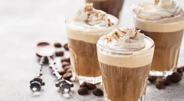 Tre bicchieri di deliziosa crema al caffè, guarniti con panna montata e cacao, circondati da chicchi di caffè.