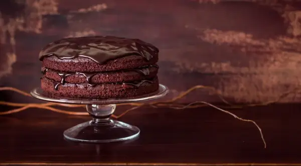 Torta a tre strati di torte al cioccolato, ricoperta da glassa lucida al cioccolato, su un'alzata di vetro.