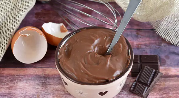 Crema pasticcera al cioccolato, liscia e invitante, pronta per essere gustata. Uova, frusta e cioccolato, ingredienti per un dolce momento.