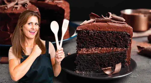 Donna sorridente con mestoli in mano, accanto a una fetta di torta tenerina Bimby, ricca e golosa.