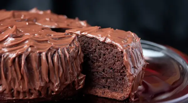 Una fetta di torta al cioccolato, soffice e umida, ricoperta da una glassa al cioccolato lucida e cremosa.