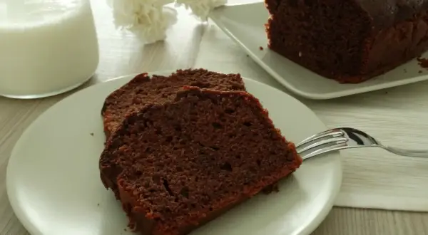 Fette di plumcake yogurt e cioccolato su un piatto, con una forchetta e un bicchiere di latte.