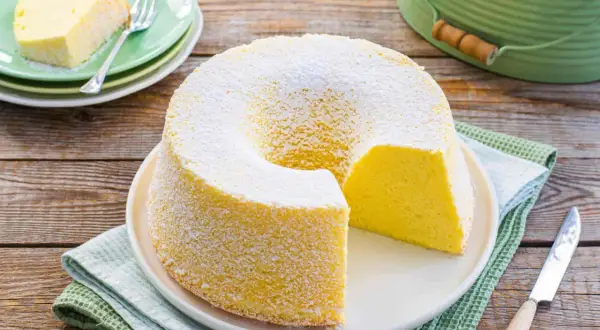 Chiffon cake ricetta originale stampo 24 cm: soffice torta gialla spolverata di zucchero a velo, una fetta servita su un piattino verde.