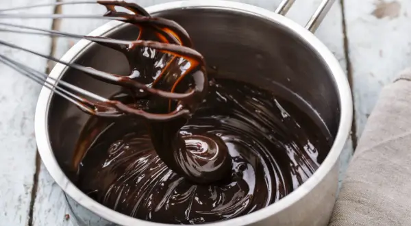 Una frusta mescola una lucida glassa al cioccolato in una pentola d'acciaio.