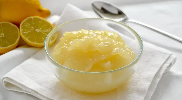 Una ciotola di cremosa crema al limone, con limoni freschi affettati sullo sfondo.