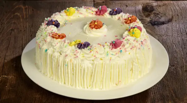 Torta compleanno uomo con panna, decorata con fiori colorati e codette, pronta per festeggiare.