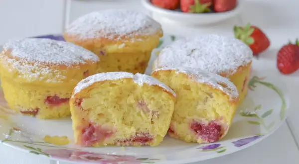 Morbidi muffin alle fragole, spolverati di zucchero a velo, invitano a un dolce assaggio. Pezzi di fragola succosa si intravedono nell'impasto soffice.