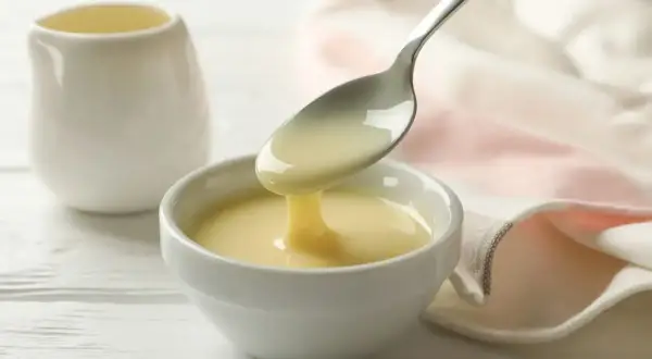 Latte condensato bimby versato da un cucchiaio in una ciotola bianca. Dolcezza cremosa pronta per dolci e caffè.