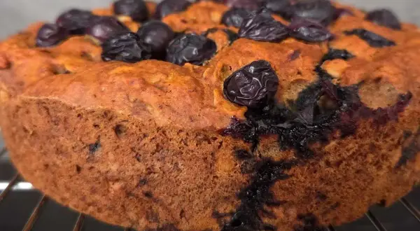Torta senza zucchero con mirtilli, dorata e soffice, appena sfornata e adagiata su una griglia.