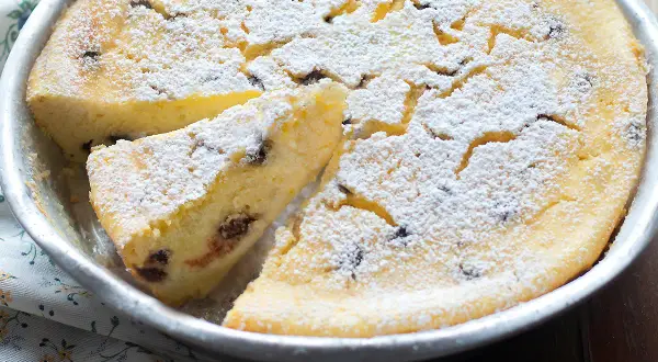 Torta soffice ricotta e cioccolato, cosparsa di zucchero a velo, in una tortiera. Una fetta è già stata tagliata.