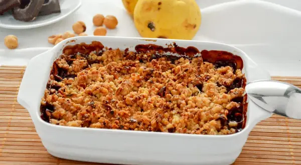 Delizioso crumble pere e cioccolato appena sfornato, con pere mature e nocciole sullo sfondo.