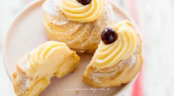 Zeppole di San Giuseppe, dolci soffici con crema pasticcera e ciliegina, uno è tagliato per mostrarne l'interno goloso.