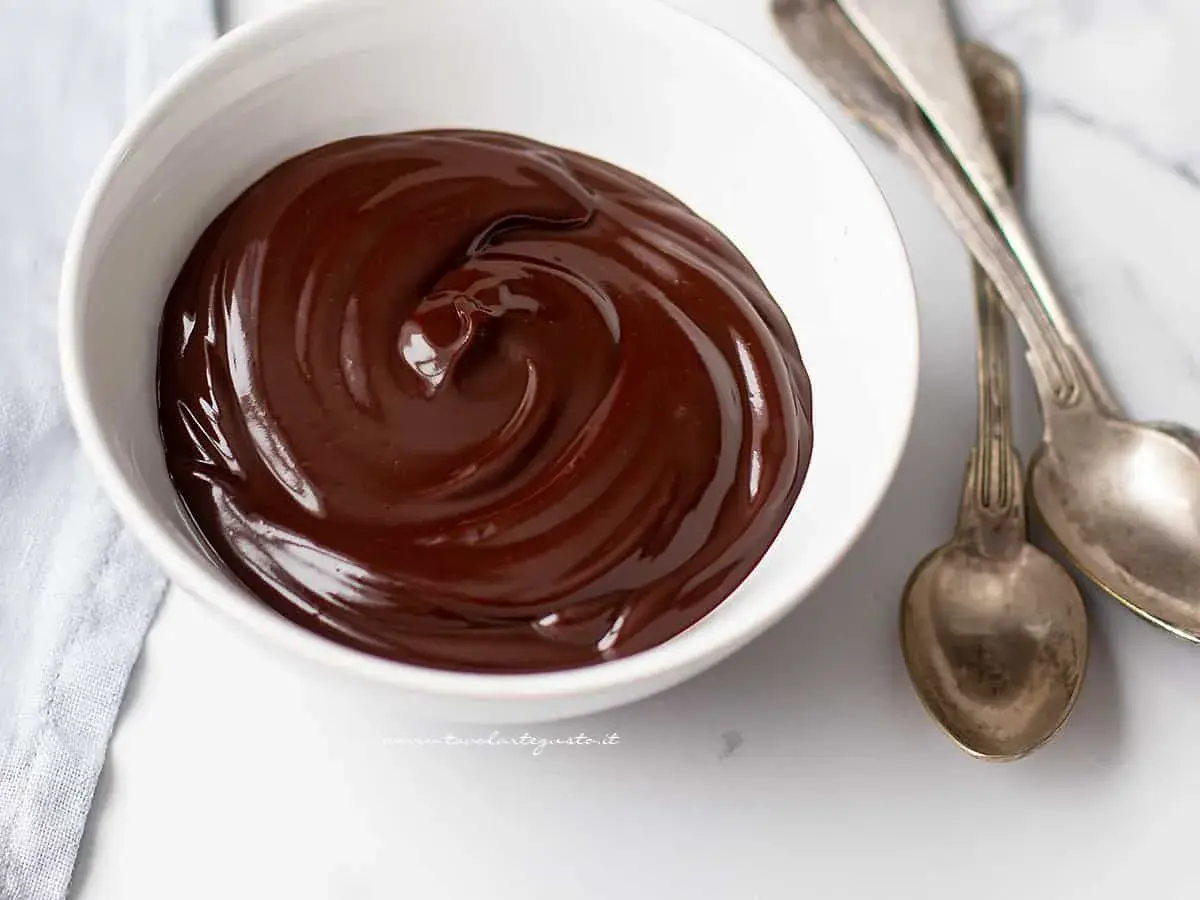 Una ciotola bianca piena di glassa al cioccolato veloce, lucida e invitante, con due cucchiai d'argento accanto.