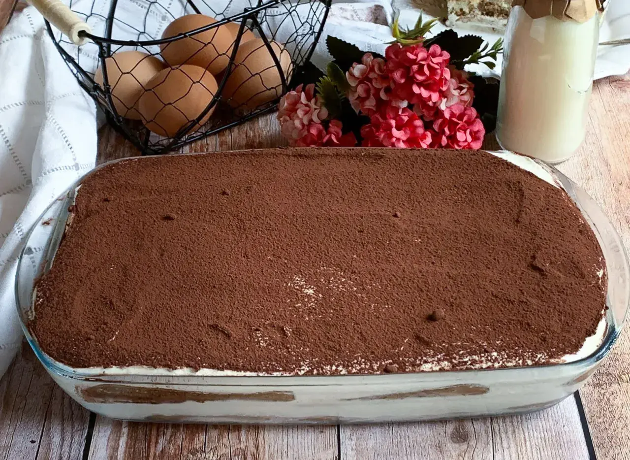 Tiramisù pronto, con 500 g di mascarpone, pronto per essere gustato. Ingredienti freschi come uova e fiori decorano la tavola.