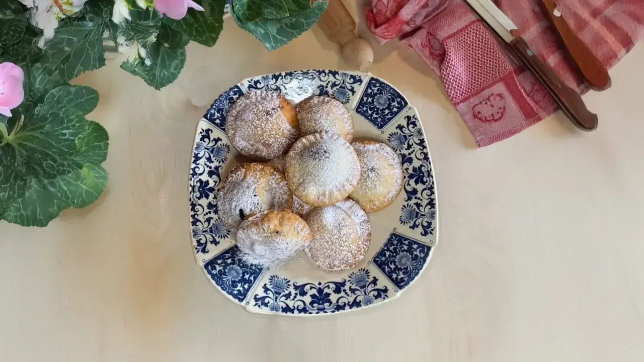 Piatto di ravioli al cioccolato spolverati di zucchero a velo, decorato con fiori e foglie verdi.