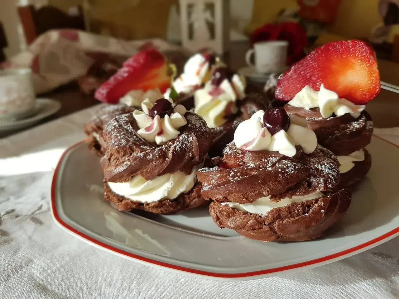 Zeppole al cacao con panna montata, ciliegie e fragole, spolverate di zucchero a velo.