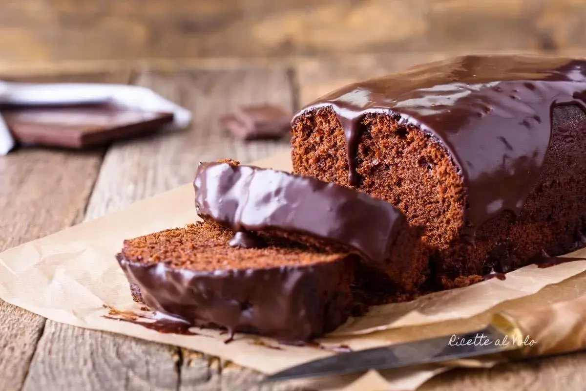 Plumcake al cioccolato con glassa lucida e due fette tagliate, su carta da forno e legno.
