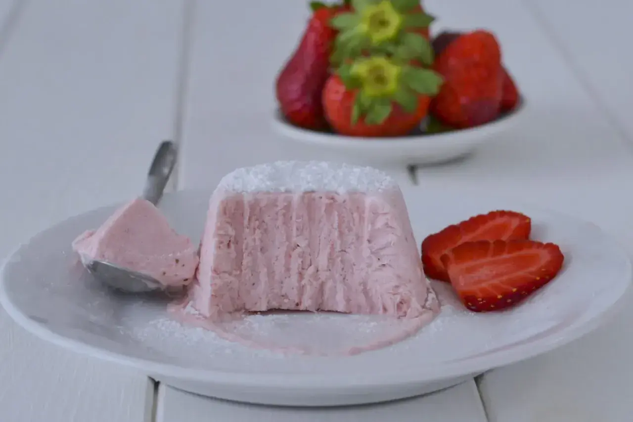 Delizioso semifreddo alle fragole, con una porzione su un cucchiaio e fragole fresche sullo sfondo.