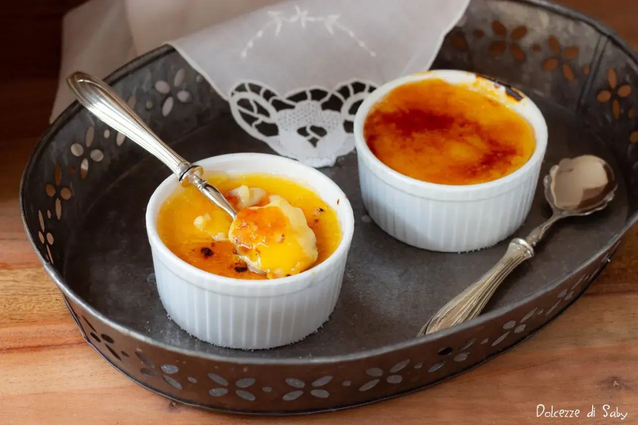 Due deliziosi creme brulee in cocotte, uno con un cucchiaino che ne assaggia la crosticina caramellata.
