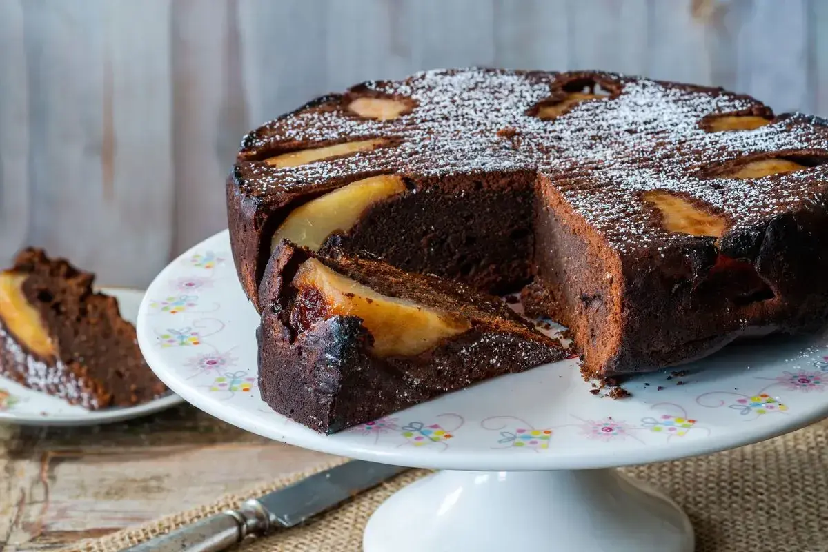 Deliziosa torta pere e cioccolato, con una fetta tagliata e cosparsa di zucchero a velo.