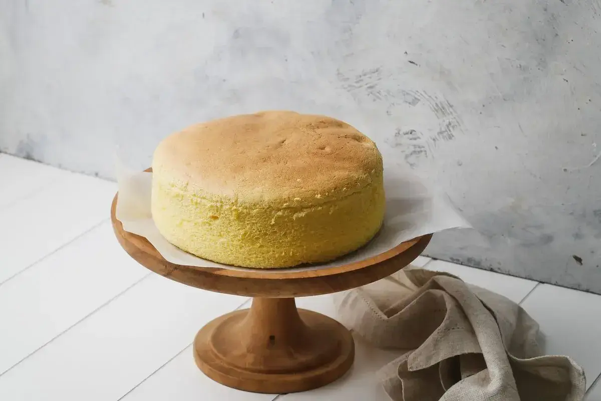 Torta soffice e dorata, preparata con albumi montati a neve, su un alzata di legno.