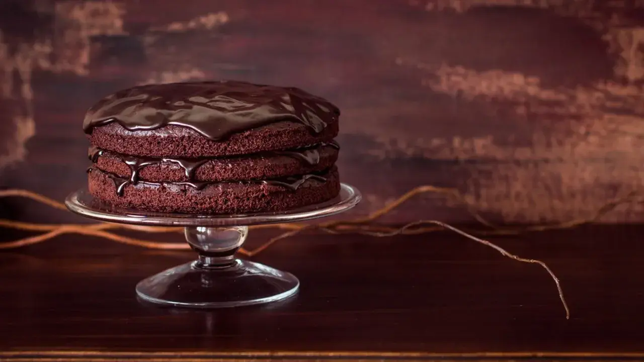 Torta a tre strati di torte al cioccolato, ricoperta da glassa lucida al cioccolato, su un'alzata di vetro.