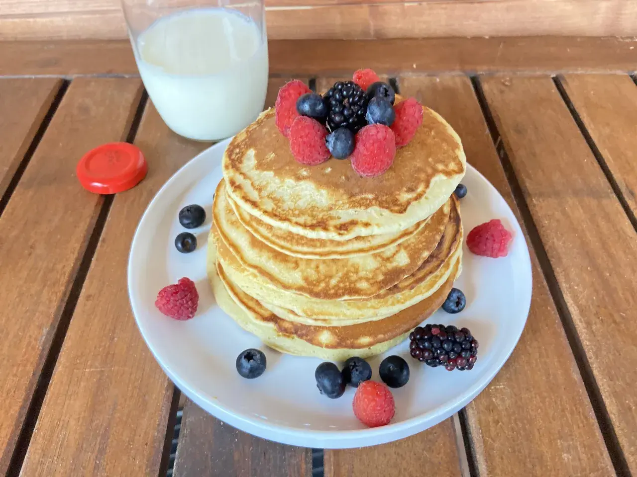 Pancake light con frutti di bosco e un bicchiere di latte su un tavolo di legno.