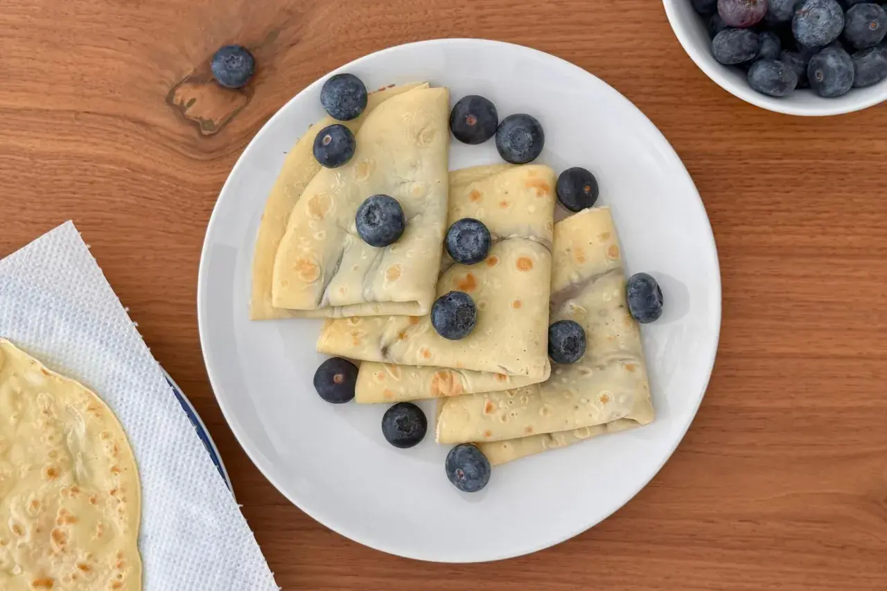 Deliziose crepes all'acqua, piegate e guarnite con mirtilli freschi, su un piatto bianco.
