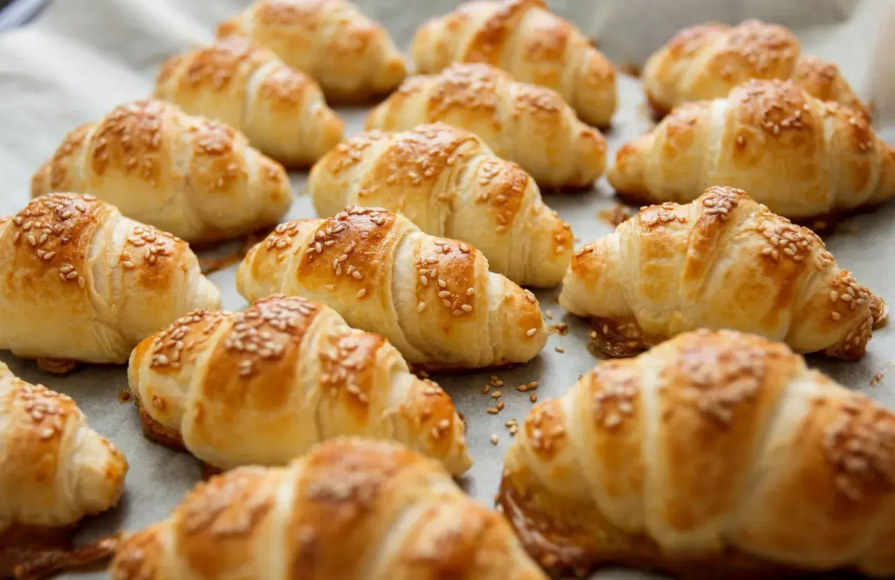 Croissant dorati e fragranti, preparati con pasta sfoglia e cosparsi di semi di sesamo, pronti per essere gustati.