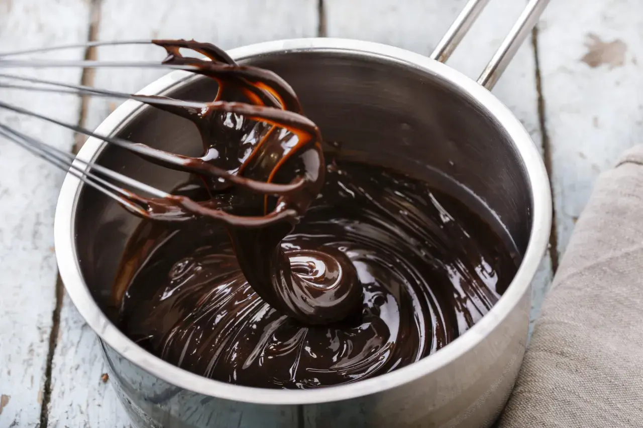 Una frusta mescola una lucida glassa al cioccolato in una pentola d'acciaio.